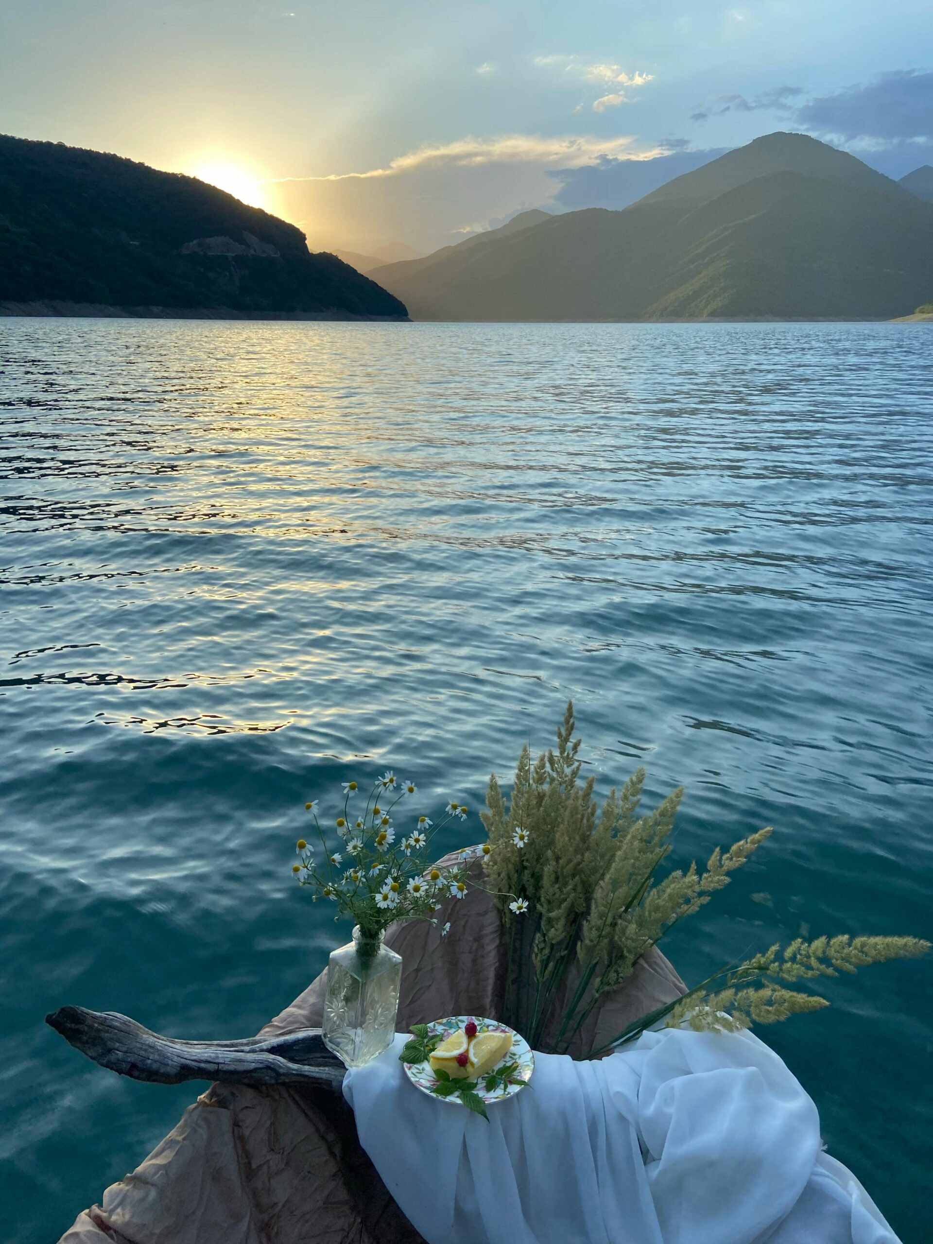 Peaceful lake view at sunset with flowers and leaves on a boat, embodying tranquility.