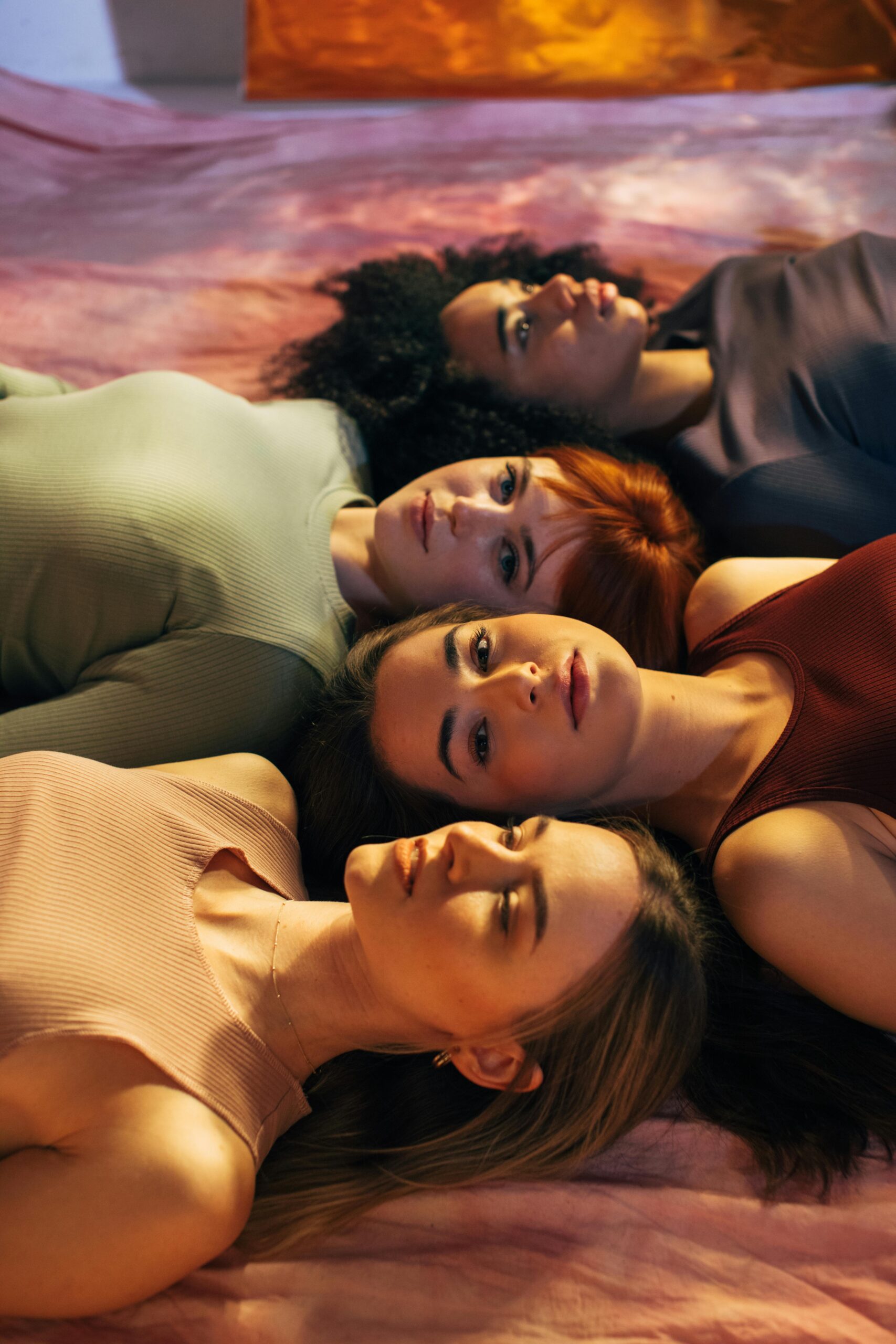 A creative studio shot featuring four diverse women lying down in a conceptual setting.